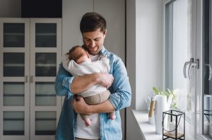 Ein friedliches Familienporträt im Lebensstil-Stil, das einen Vater zeigt, der sein Baby liebevoll in seinen Armen hält.