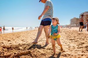 Natürliches Strandfotoshooting mit kleinem Mädchen, das im Sand tanzt