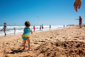 Natürliches Strandfotoshooting mit kleinem Mädchen, das Sand hochhält